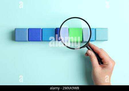 Femme tenant une loupe au-dessus des cubes colorés sur fond bleu clair, vue de dessus. Concept de recherche Banque D'Images