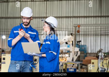 Une équipe d'ingénieurs hommes et femmes se réunit pour inspecter les robots de soudage de l'acier commandés par ordinateur. Planifier les répétitions et l'installation pour l'utilisation. Banque D'Images