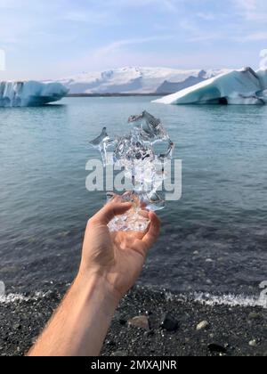 Main tenant de la glace, derrière des flotteurs de glace sur le lagon du glacier, Joekulsarlon, lac glaciaire, bord sud de Vatnajoekull, sud-est de l'Islande, Islande Banque D'Images