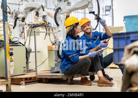 Une équipe d'ingénieurs hommes et femmes se réunit pour inspecter les robots de soudage de l'acier commandés par ordinateur. Planifier les répétitions et l'installation pour l'utilisation. Banque D'Images