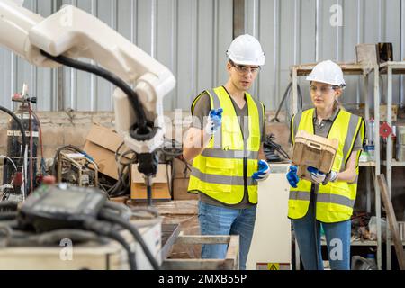 Une équipe d'ingénieurs hommes et femmes se réunit pour inspecter les robots de soudage de l'acier commandés par ordinateur. Planifier les répétitions et l'installation pour l'utilisation. Banque D'Images