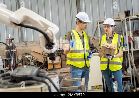 Une équipe d'ingénieurs hommes et femmes se réunit pour inspecter les robots de soudage de l'acier commandés par ordinateur. Planifier les répétitions et l'installation pour l'utilisation. Banque D'Images
