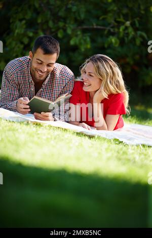 Parfait après-midi dans le parc. un jeune couple heureux lisant un livre tout en étant allongé sur l'herbe dans un parc. Banque D'Images