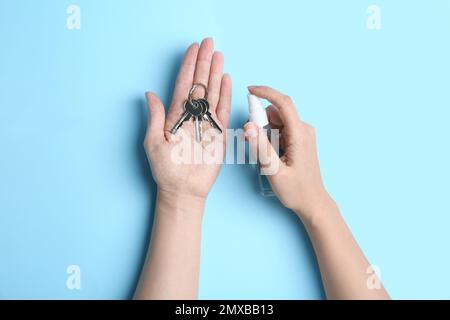 Femme pulvérisant un antiseptique sur des clés sur fond bleu clair, vue de dessus Banque D'Images