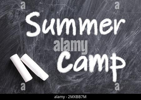 Morceaux de craie blanche et texte CAMP D'ÉTÉ écrit sur tableau noir, plat Banque D'Images