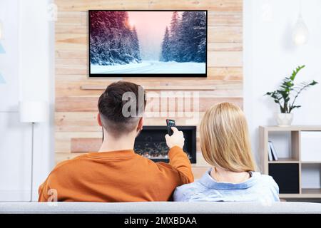 Couple regardant la télévision sur le canapé dans la salle de séjour avec cheminée décorative Banque D'Images