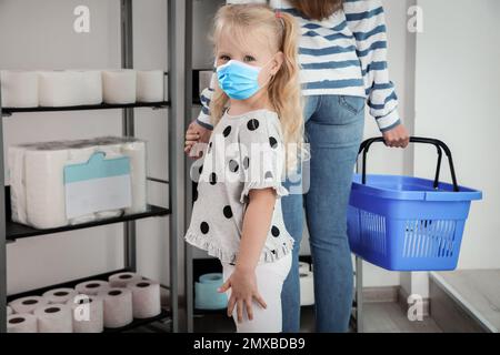 Petite fille avec masque médical et mère achetant du papier toilette en magasin Banque D'Images