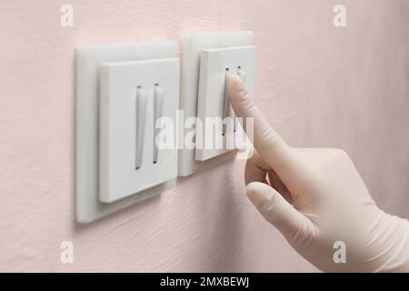 Femme en gants de protection en appuyant sur le bouton de l'interrupteur d'éclairage à l'intérieur, gros plan Banque D'Images