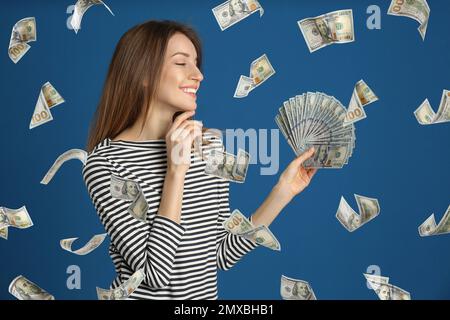 Femme avec des dollars américains sous la pluie d'argent sur fond bleu Banque D'Images