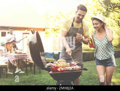 Un jeune homme et une jeune femme près d'un barbecue à l'extérieur par beau temps Banque D'Images