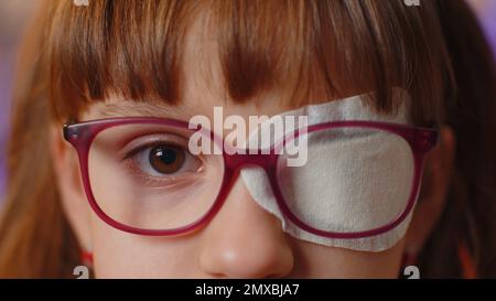 Gros plan portrait de malade visage de fille regardant l'appareil photo, ayant le pansement protecteur patch raye sur un oeil. Blessures, aveugles. Enfant en lunettes. Correction médicale de la thérapie de la vue Banque D'Images