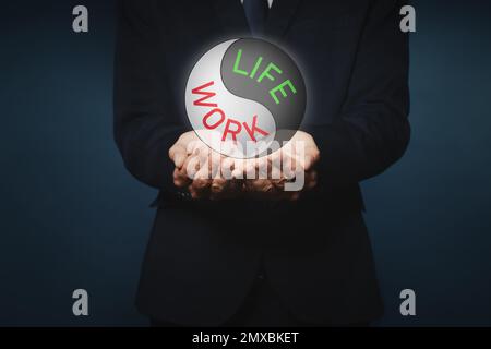 Homme d'affaires montrant l'équilibre entre la vie et le travail sur fond sombre, gros plan Banque D'Images