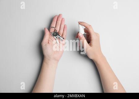 Femme pulvérisant un antiseptique sur des clés sur fond gris clair, vue de dessus Banque D'Images