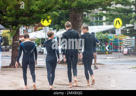 Quatre jeunes garçons adolescents vêtues de combinaisons marchant le long de la promenade à Manly Beach, Sydney, Nouvelle-Galles du Sud, Australie Banque D'Images