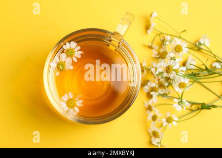 Tasse de thé et fleurs de camomille sur fond jaune, plat Banque D'Images