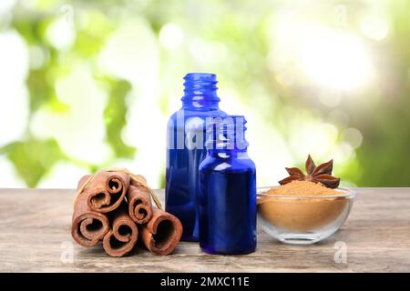 Bouteilles d'huile essentielle, bâtonnets de cannelle et poudre sur table en bois sur fond flou Banque D'Images