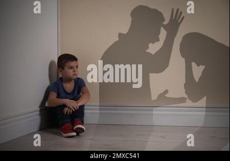 Petit garçon assis dans le coin près du mur jaune et silhouettes de parents argumenteurs Banque D'Images