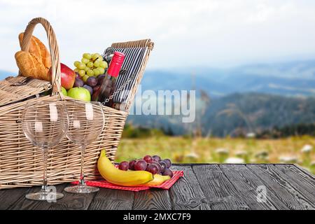 Panier pique-nique en osier avec vin et différents produits sur table en bois dans le parc, espace pour le texte Banque D'Images