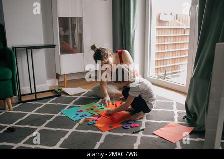 Portrait de la famille de la jeune femme et du préadolescent assis sur le sol à la maison, jouant avec des nombres colorés. Éducation. Banque D'Images