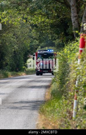 Lors d'une agréable journée d'été dans le Suffolk rural, un moteur d'incendie assiste à un grand incendie dans une petite zone industrielle. Banque D'Images