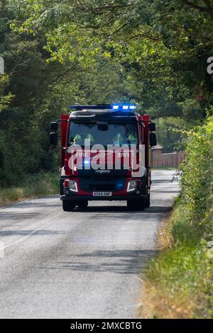 Lors d'une agréable journée d'été dans le Suffolk rural, un moteur d'incendie assiste à un grand incendie dans une petite zone industrielle. Banque D'Images