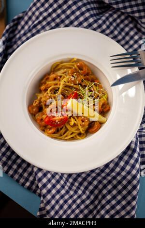 Spaghetti aux crevettes, citron et micro-vert. Déjeuner dans un plat blanc profond, gros plan. Pâtes avec fruits de mer, tomates et salade. Banque D'Images