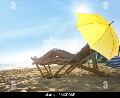 Un jeune couple se détend dans des chaises longues sous un parasol pour se protéger du soleil sur la plage près de la mer Banque D'Images