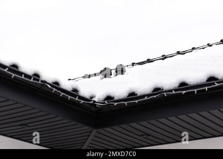 Le toit d'une maison unifamiliale est couvert de neige sur un ciel nuageux, d'une cheminée de ventilation en céramique visible sur le toit et de neige tombant. Banque D'Images