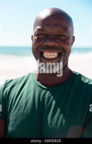 Portrait en gros plan d'un homme senior afro-américain chauve-souris gai souriant à la plage dans un ciel dégagé Banque D'Images