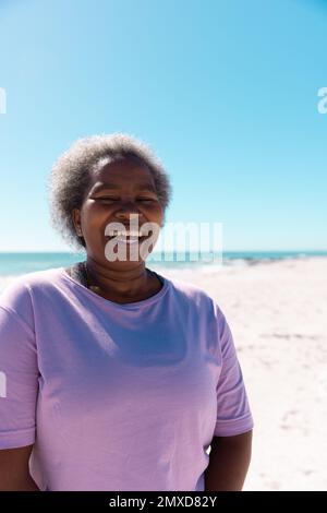 Femme africaine américaine senior avec de courts cheveux gris riant à la plage contre le ciel clair le jour ensoleillé Banque D'Images