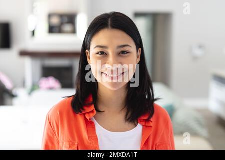 Portrait d'une heureuse femme biraciale souriant dans le salon à la maison, avec espace de copie. Concept de loisirs, de bonheur et de vie domestique. Banque D'Images