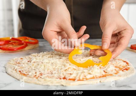 Femme ajoutant du poivron à la table en marbre blanc de pizza, gros plan Banque D'Images