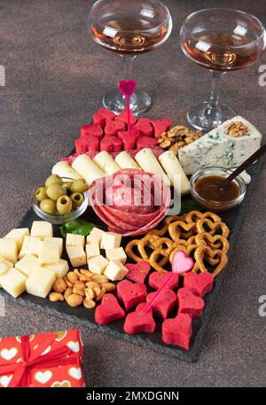 Carte de charcuterie pour la Saint-Valentin avec différentes variétés de saucisse, fromage, noix, olives et deux verres de vin rose, image verticale Banque D'Images