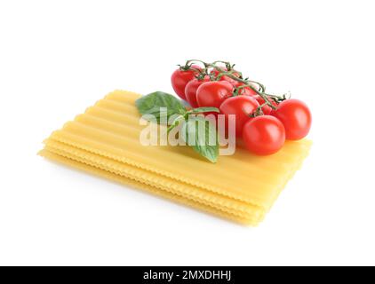 Feuilles de lasagne non cuites, tomates cerises et basilic isolés sur blanc Banque D'Images