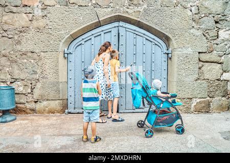 Les membres de la famille marchent ensemble et essaient de regarder à travers la porte en bois dans le mur de pierre. Les touristes passent des vacances dans la ville de la station et explorer les destinations Banque D'Images