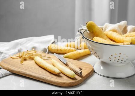 Carottes blanches brutes, couteau et planche à découper sur une table en marbre gris clair Banque D'Images