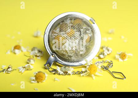 Sécher les fleurs de camomille dans l'infuser sur fond jaune, gros plan Banque D'Images