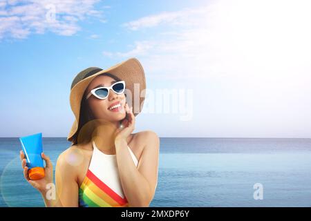 Jeune femme avec crème solaire près de la mer, espace pour le texte Banque D'Images
