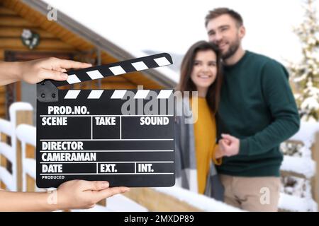 Assistant tenant un clapperboard et un jeune couple à l'extérieur le jour de neige, en gros plan. Production cinématographique Banque D'Images