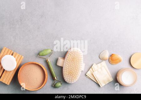 Ensemble de produits de soin et de bien-être pour la peau. Brosse de massage, rouleau de jade, tampons de coton, savon, masque d'argile facial sur fond de pierre grise. Banque D'Images