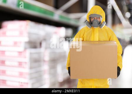 Homme portant une combinaison de protection contre les produits chimiques avec une boîte en carton en magasin. Marché de gros Banque D'Images