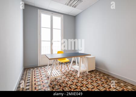 Une chambre vide avec des murs gris lisses, des portes menant à la terrasse. Le sol est fait de carreaux de marbre à motifs. Il y a une table avec un dessus gris et un plastique jaune Banque D'Images