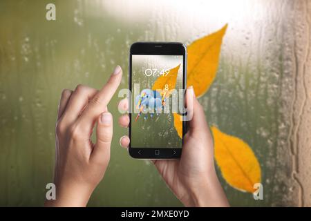 Femme utilisant l'application de prévisions météorologiques sur smartphone près d'une fenêtre à l'intérieur, en gros plan Banque D'Images