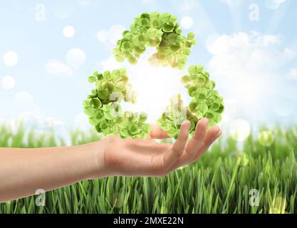 Homme avec symbole de recyclage fait de feuilles à l'extérieur, gros plan Banque D'Images