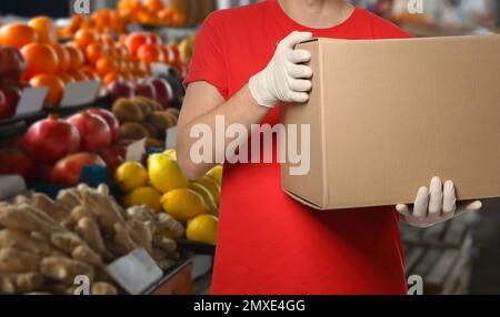 Homme avec boîte en carton contre les fruits frais dans le magasin, fermer. Marché de gros Banque D'Images