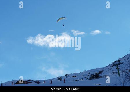 Paraskier sur un parachute descendant de Val Thorens dans la vallée des Menuires dans les alpes françaises - éclairé par le soleil matinal sur un ciel bleu. Banque D'Images