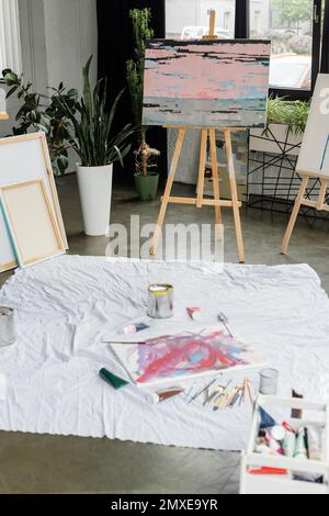 Peinture sur chevalet à proximité de peintures et pinceaux sur tissu en studio, image de stock Banque D'Images