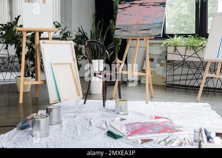 Toiles à proximité de peintures et de pinceaux sur le sol en studio, image de stock Banque D'Images