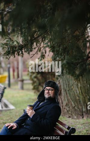 Un homme âgé bénéficie d'un matin d'hiver froid dans la ville. Un homme est assis sur un banc sur la place, le concept de paix et de vitalité. Banque D'Images