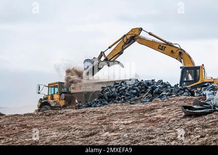 Une pelle hydraulique charge les déchets solides dans un grand conteneur de camion pour transporter une grande quantité de poussière dans une décharge active. Banque D'Images